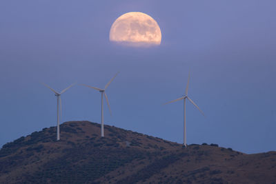 Landscape of some windmills on a mountain with the moon in the background