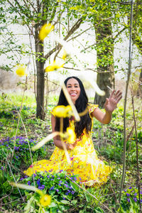 Mixed race african american woman in a yellow dress sits in wildflowers and tosses dandelions