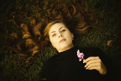 High angle portrait of holding flowers while lying on grassy field