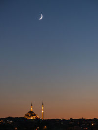 Moon over illuminated mosque against clear sky at night