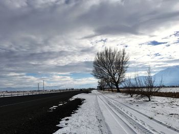 Road by snowy field against cloudy sky