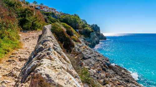 Scenic view of rocks by sea against clear blue sky