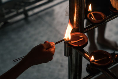 Close-up of human hand holding burning incense sticks from oil lamp