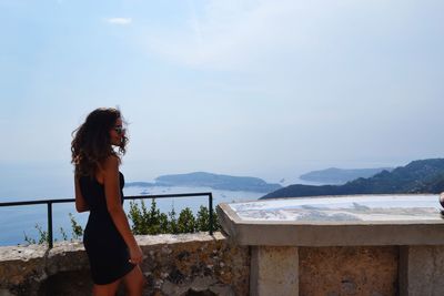 Woman standing by retaining wall against sky