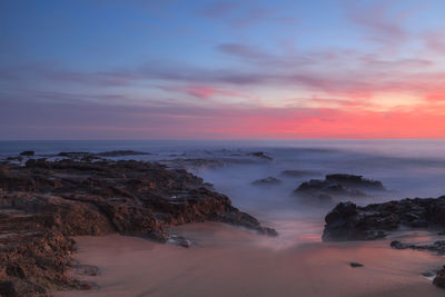 Rock formations in sea against cloudy sky during sunset