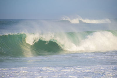 Waves rushing towards shore against sky