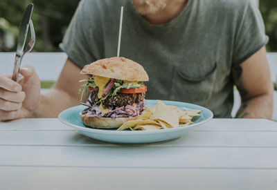 Midsection of man eating burger and potato chips while sitting at table in yard