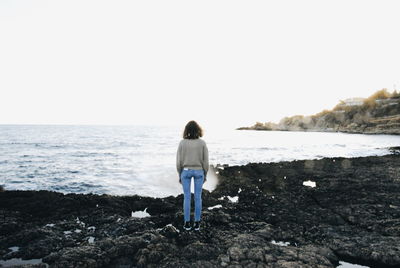 Rear view of teenage girl looking at sea against clear sky