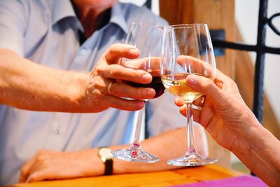 Midsection of man toasting wine woman while sitting at table