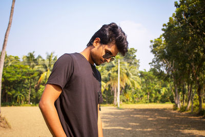 Side view of young man looking away against trees