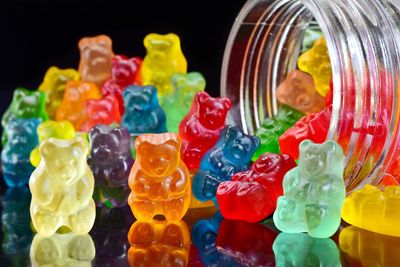 Close-up of multi colored gummi bears spilling from glass jar over black background