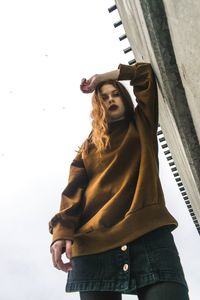 Low angle view of woman standing by wall against sky