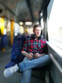 Handsome man sitting in bus with mobile phone and headphones looking away