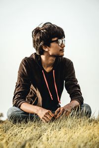 Young man looking away while sitting on field