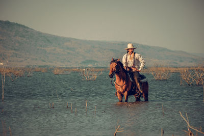 Full length of man sitting on horse in river against sky