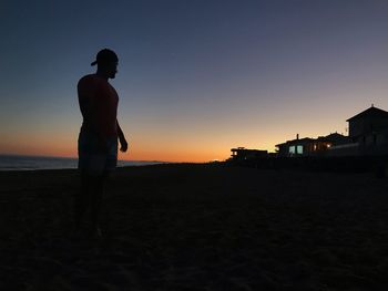 Silhouette man standing on beach against sky during sunset