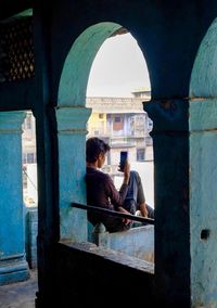 Rear view of man using mobile phone while sitting outside building