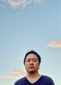 Portrait of young asian man standing against pink clouds in blue sky at sunset.