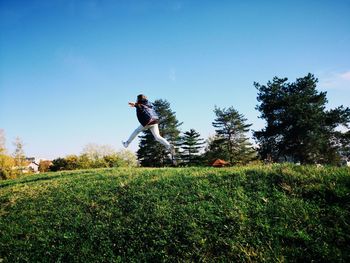 Man jumping on field against clear sky