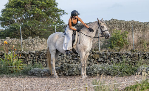 White lusitano mare, female dressage rider, outdoors on sand.