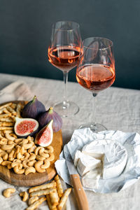 Rose wine with ripe figs, camembert cheese and cashews on a table indoors.