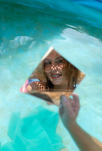 Young woman holding mirror with reflection in wading pool