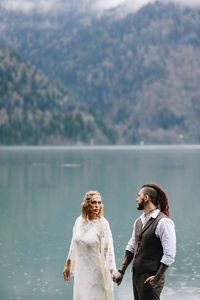 Two happy people in love the bride and groom in wedding outfits embrace by the lake and mountains