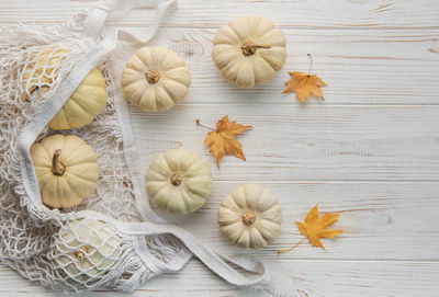 Top view autumn composition with pumpkins in mesh shopping bag on a wooden background