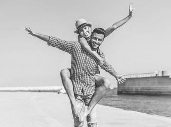 Portrait of smiling young man with girlfriend on back by sea