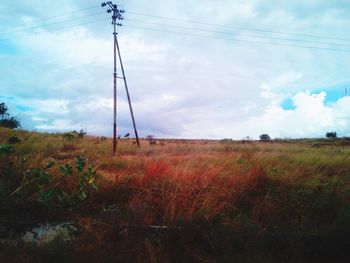 Electricity pylon on field against cloudy sky