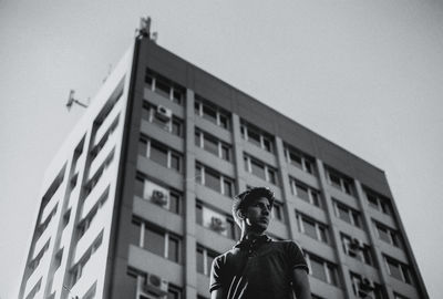 Low angle portrait of man standing against building against clear sky