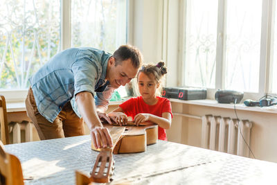 Father and daughter repairing guitar on table at home