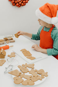A boy in a santa hat lays out ginger cookies on the kitchen table. new year's eve.