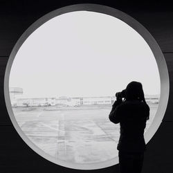 Woman photographing from circular window at airport