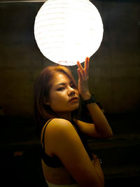Portrait of young woman looking at illuminated lamp