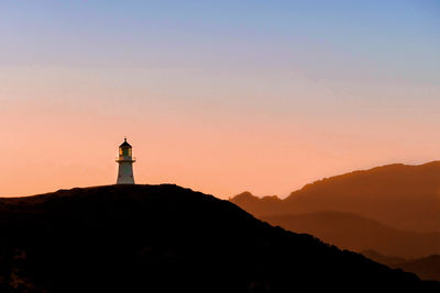 Lighthouse on mountain against clear sky at sunset