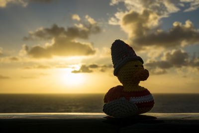 Close-up of figurine on beach against sky during sunset