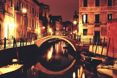 Arch bridge over canal amidst buildings in city at night