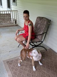 Young woman stroking dog while sitting on chair at porch