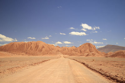 Dirt road leading towards mountains against sky