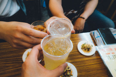 Cropped hands of friends holding drink over table