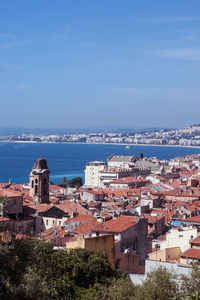 High angle view of townscape by sea against blue sky