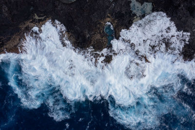 Beautiful drone shot of waves gently breaking on the shore with rocks, with blue color from above