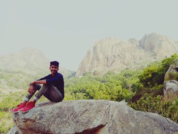 Young man sitting on rock against mountains