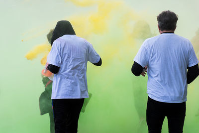 Rear view of people standing against yellow wall