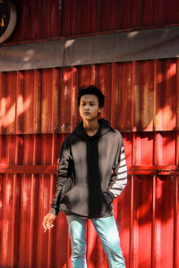 Portrait of young man standing against red curtain