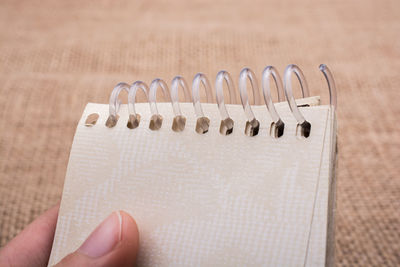 Close-up of human hand holding spiral notebook by burlap