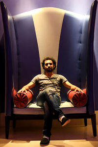 Portrait of young man sitting on chair in illuminated room