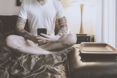 Midsection of man using mobile phone while sitting on sofa
