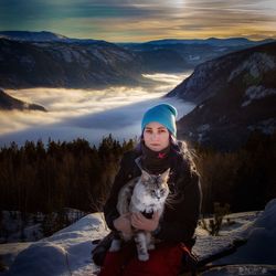 Woman holding cat while sitting against snowy mountains